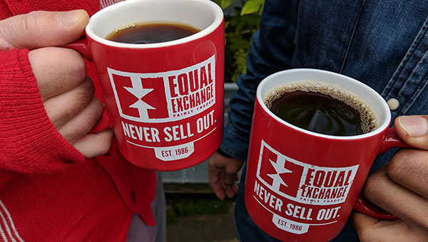 Two people holding two red Equal Exchange mugs